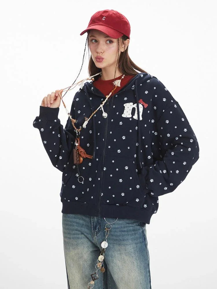 Close-up of a woman wearing a navy blue zip-up hoodie with a white paw print pattern and an embroidered graphic