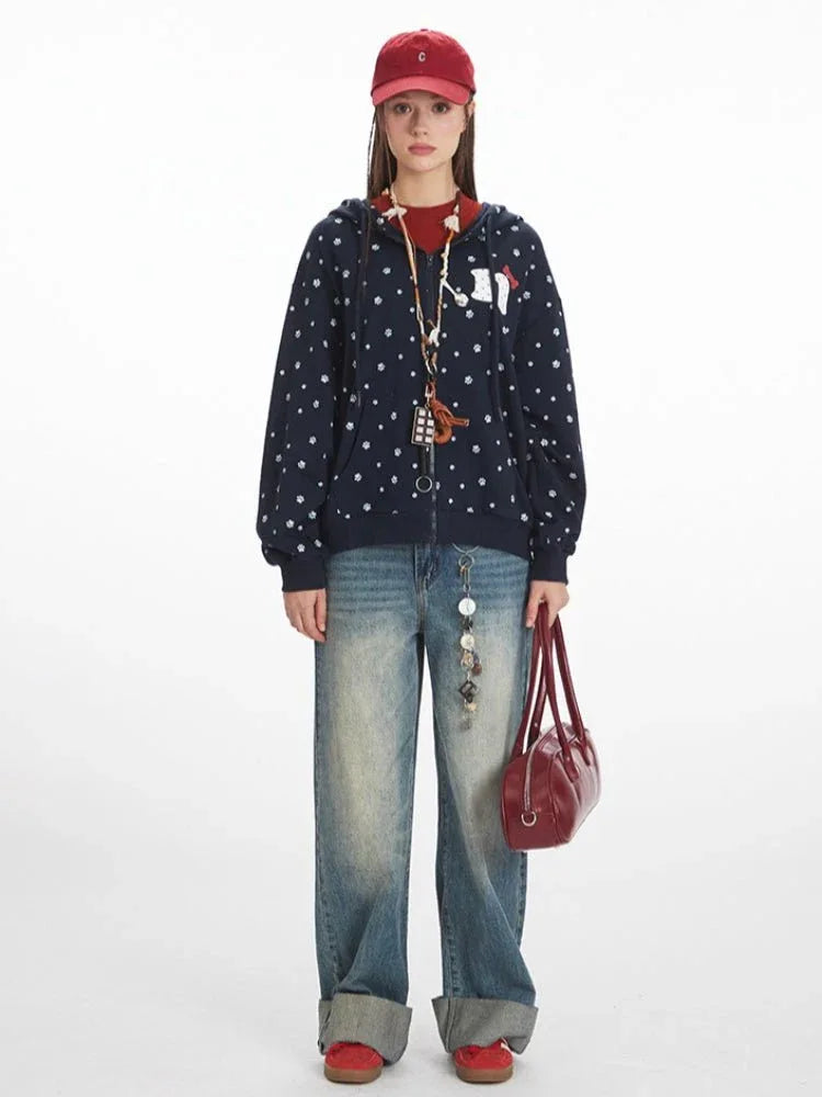 Woman wearing a navy blue zip-up hoodie with a white paw print pattern and a red baseball cap