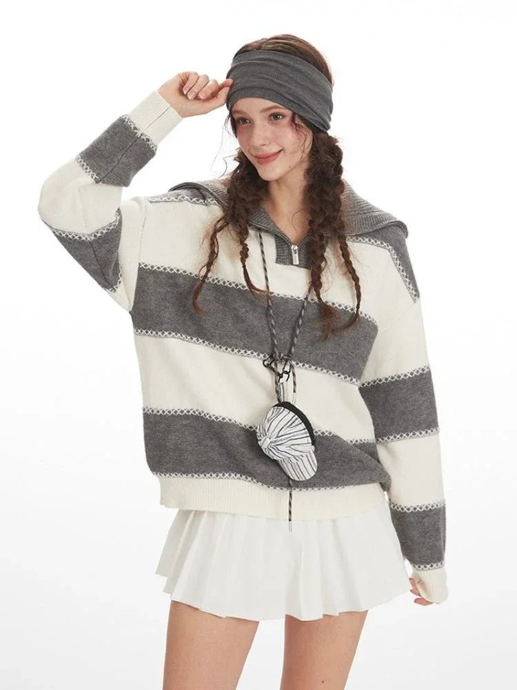 Close-up of a woman wearing a grey and white striped knit sweater with a spread collar and zipper closure, accessorized with a headband and a small circular bag.