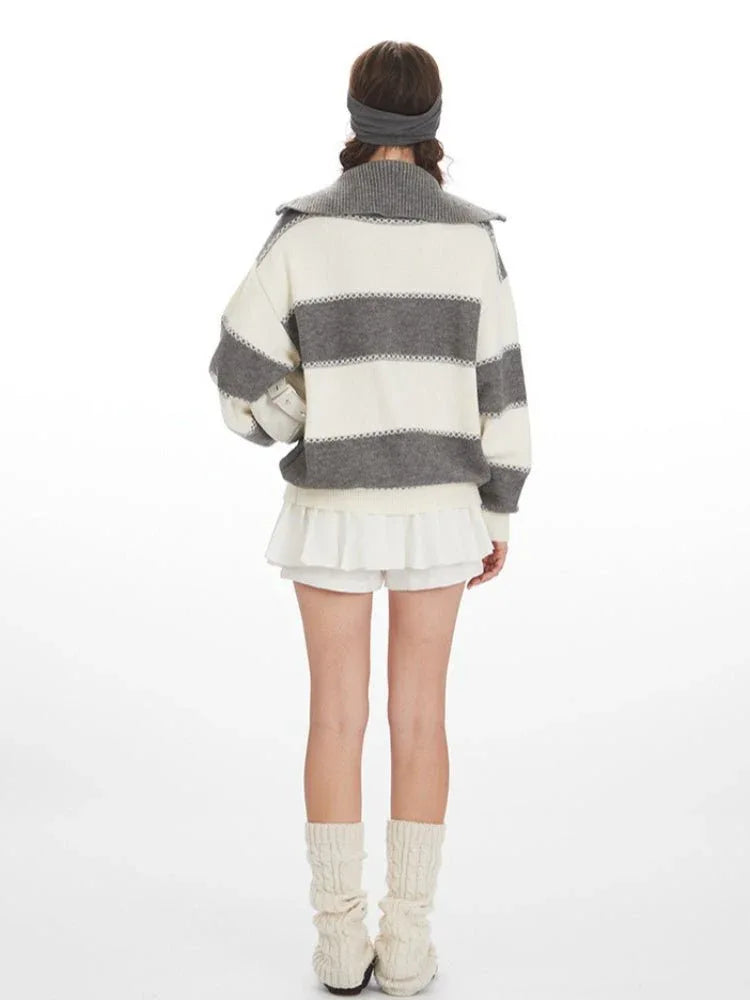 Woman wearing a grey and white striped knit sweater with a spread collar and zipper closure, paired with a white pleated skirt and leg warmers.