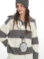 Front detail of a woman wearing a grey and white striped knit sweater with a spread collar and zipper closure, highlighting the knit texture and stripes.