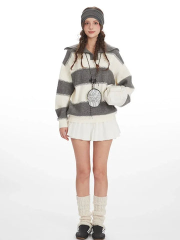 Woman wearing a grey and white striped knit sweater with a spread collar and zipper closure, paired with a white pleated skirt and leg warmers.