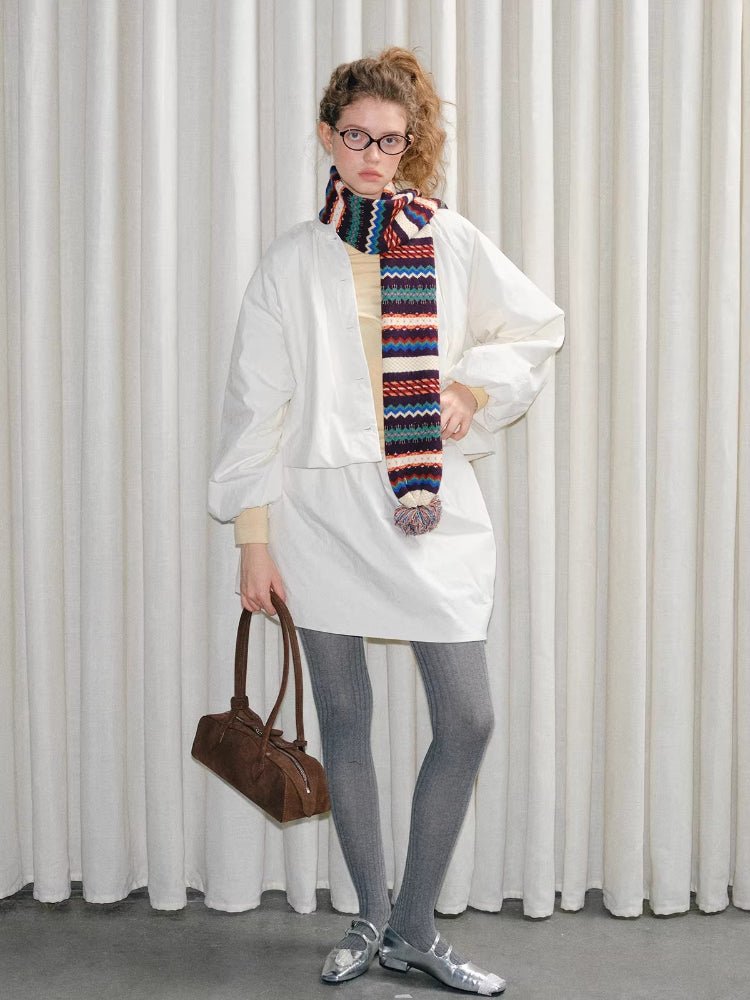 Woman posing with a white outfit, patterned scarf, and brown shoulder bag.