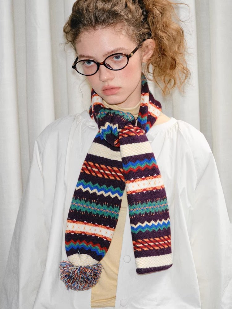 Woman wearing a white jacket and a colorful patterned scarf with a pom-pom.