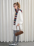 Full body shot of a woman in a white outfit, holding a brown handbag and wearing a colorful scarf.