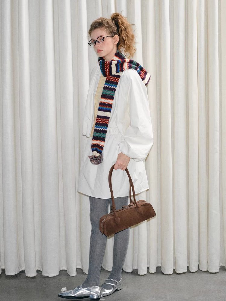 Full body shot of a woman in a white outfit, holding a brown handbag and wearing a colorful scarf.