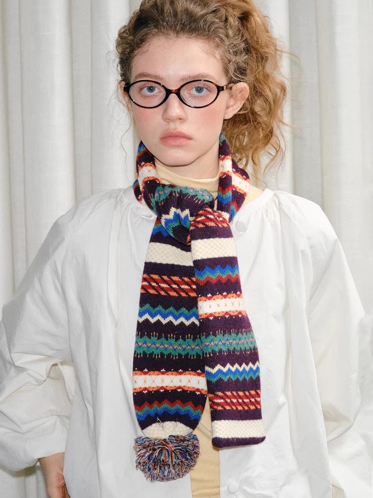 Woman wearing a white jacket and a colorful patterned scarf with a pom-pom.