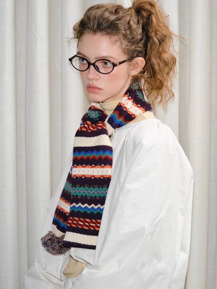 Woman with curly hair and glasses wearing a white jacket and a striped knit scarf.