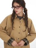 Front detail of a woman's tan button-up shirt, highlighting the embroidered logo and plaid cuff.