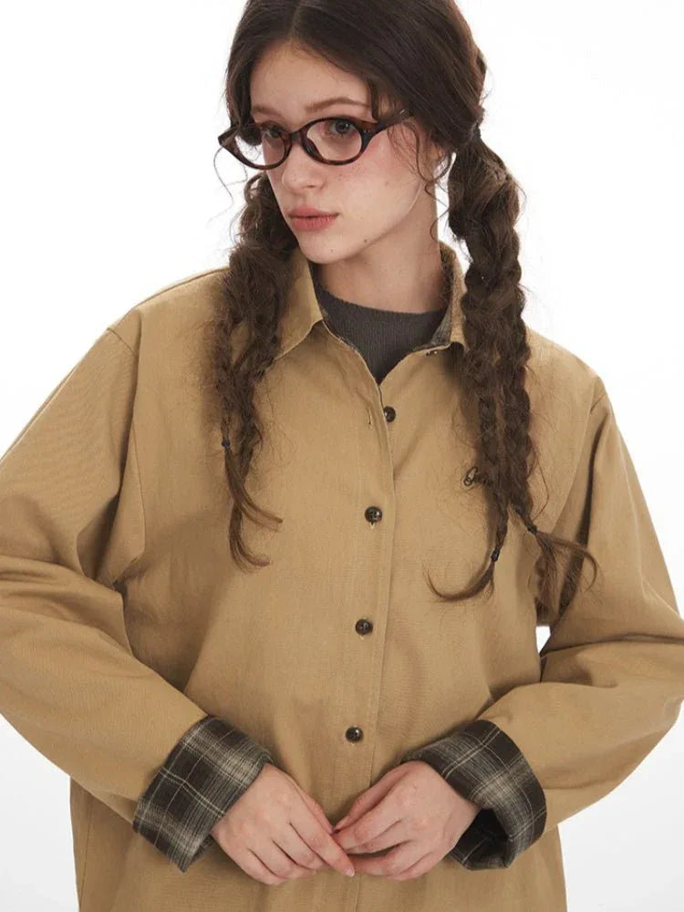 Front detail of a woman's tan button-up shirt, highlighting the embroidered logo and plaid cuff.