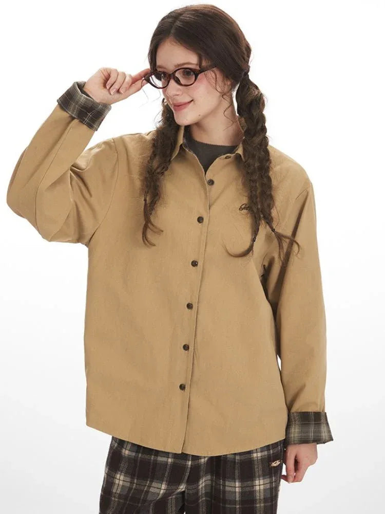 Close-up of a woman wearing a tan button-up shirt, showing the collar, buttons, and plaid cuff detail.