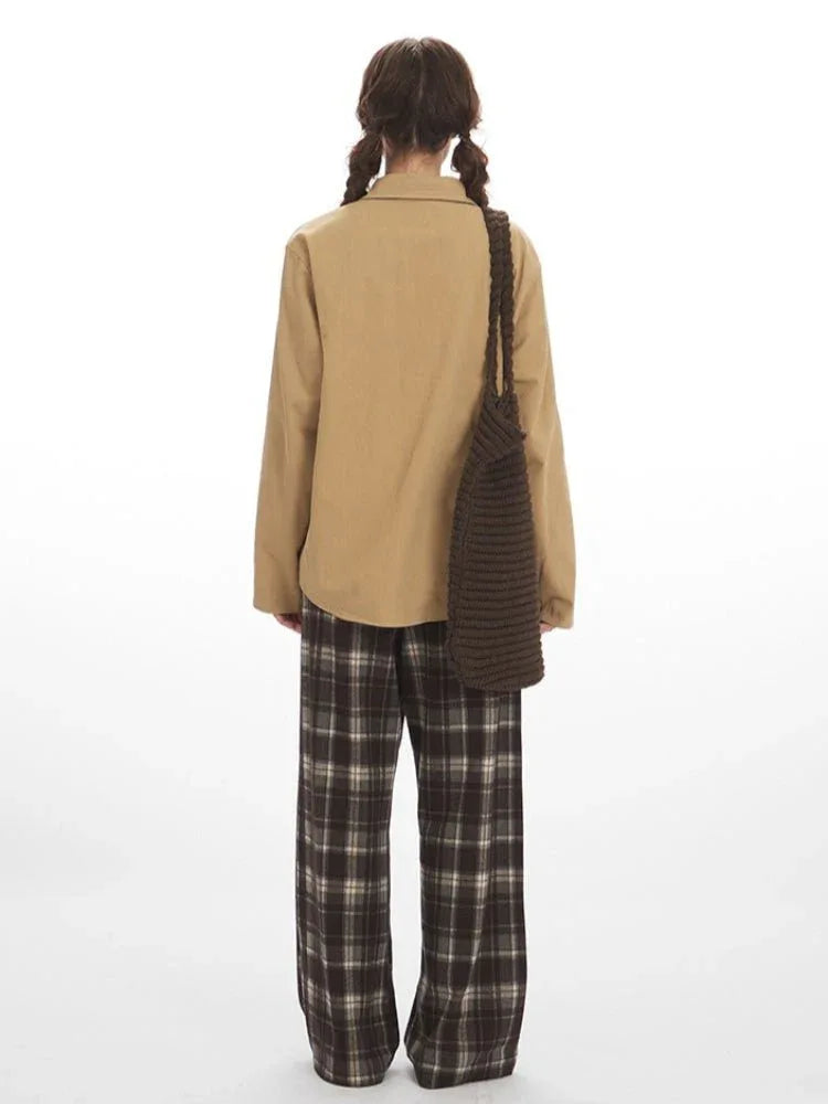 Back view of a woman wearing a tan button-up shirt with plaid trim and brown plaid wide-leg pants.