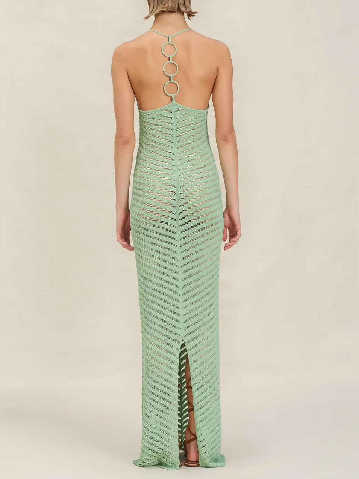 Back view of a woman in a mint green knit maxi dress with an open back and ring details