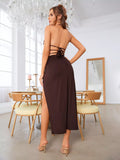 Back view of a woman wearing a brown halter neck bikini top with tie closures and a high-slit maxi skirt with a ring detail, standing in a dining room.