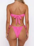 Woman wearing a bright pink strapless bikini top with a bow detail at the bust and matching bikini bottoms with adjustable side ties, back view.