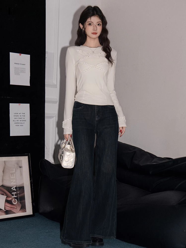 Full body shot of a woman in a white long-sleeve knit top and dark wash flared jeans.