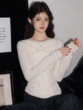 Woman wearing a white long-sleeve fitted knit top with ruffle trim and beaded embellishments on the neckline and cuffs.