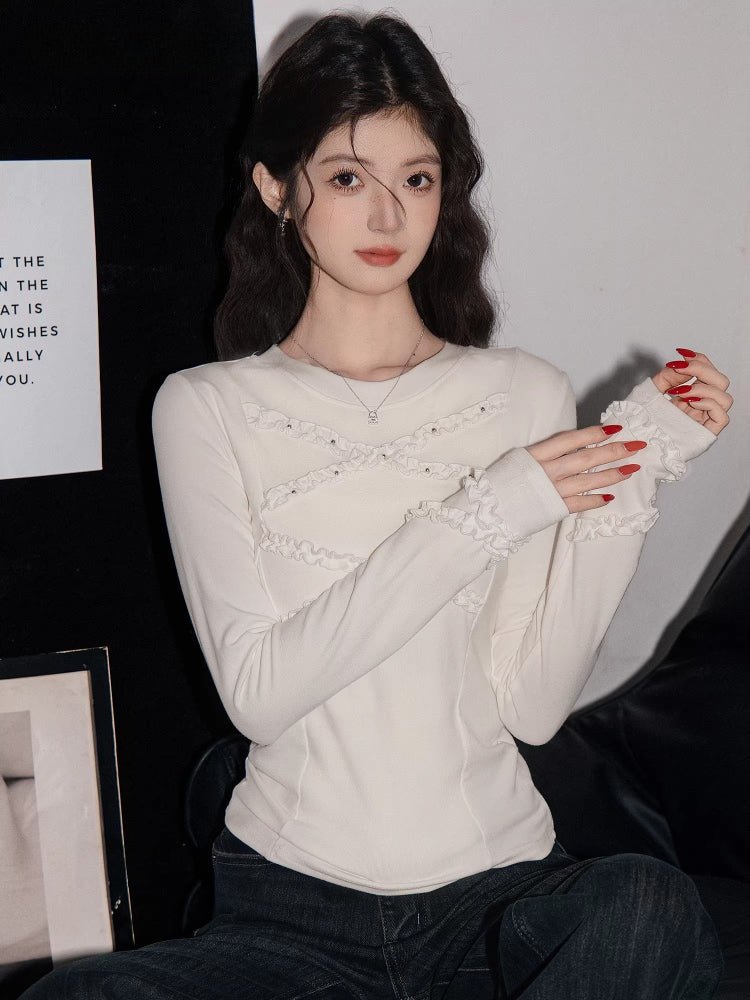 Woman wearing a white long-sleeve fitted knit top with ruffle trim and beaded embellishments on the neckline and cuffs.