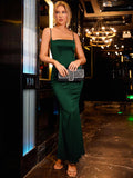 Woman in a floor-length emerald green satin mermaid dress, holding a beaded clutch bag.