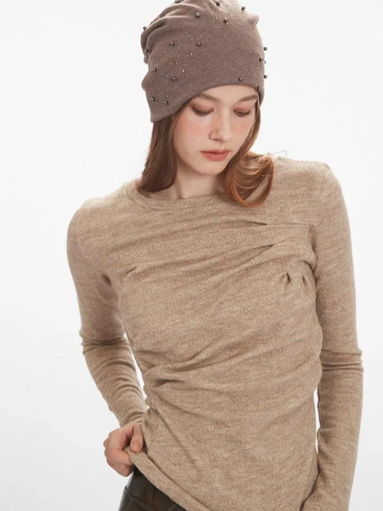 Front view of a woman in a tan knit top with ruching and draping on the bodice.