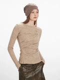 Close-up of a woman wearing a tan knit top with intricate draping across the chest and a round neckline.