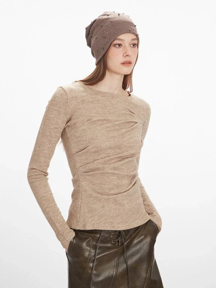 Close-up of a woman wearing a tan knit top with intricate draping across the chest and a round neckline.
