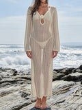 Woman wearing a cream crochet maxi cover-up dress with long sleeves and a deep V-neckline over a bikini on a rocky beach.