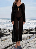 Woman wearing a black crochet maxi cover-up dress with long sleeves and a deep V-neckline over a black bikini on a rocky beach.