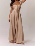 Woman wearing a beige linen blend jumpsuit with a strappy bralette top and wide legs, side view showing draped fabric