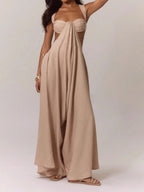 Woman wearing a beige linen blend jumpsuit with a strappy bralette top and wide legs, side view showing draped fabric