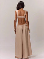 Woman wearing a beige linen blend jumpsuit with a strappy bralette top and wide legs, back view showing open back and smocked waistband
