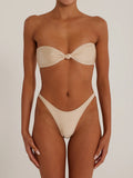 Woman modeling a beige strapless bikini top with a knot detail and matching high-cut bottoms