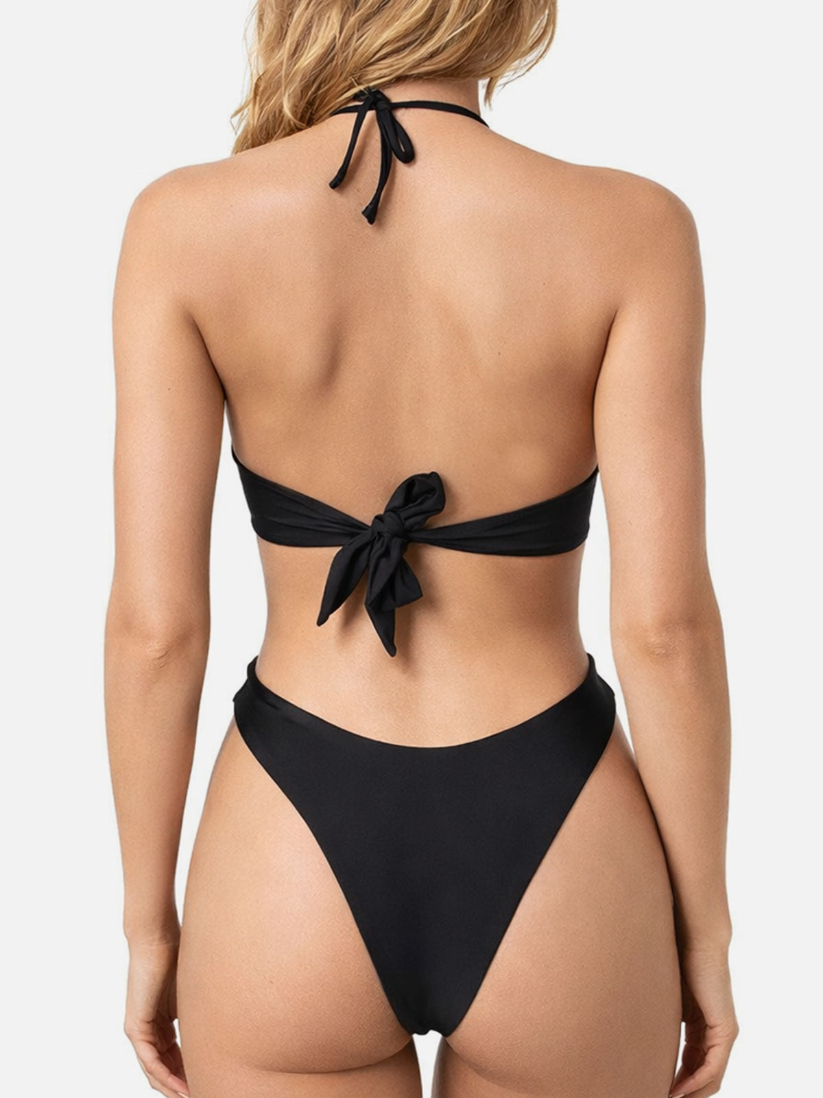 Back view of a woman wearing a black bikini with a halter top and high-cut bottoms.