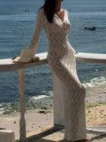 Woman wearing a cream knit maxi dress with a deep V-neck and bell sleeves, standing on a balcony overlooking the ocean.