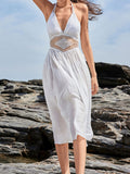 Woman wearing a white halter neck maxi dress with lace waist detail on a rocky beach