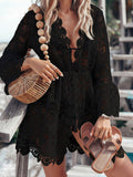 Woman wearing a black lace cover-up with bell sleeves and a deep V-neckline, holding a straw bag and sandals.