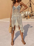 Woman wearing a cream crochet cover-up dress with spaghetti straps and an asymmetrical hem, holding a straw bag.