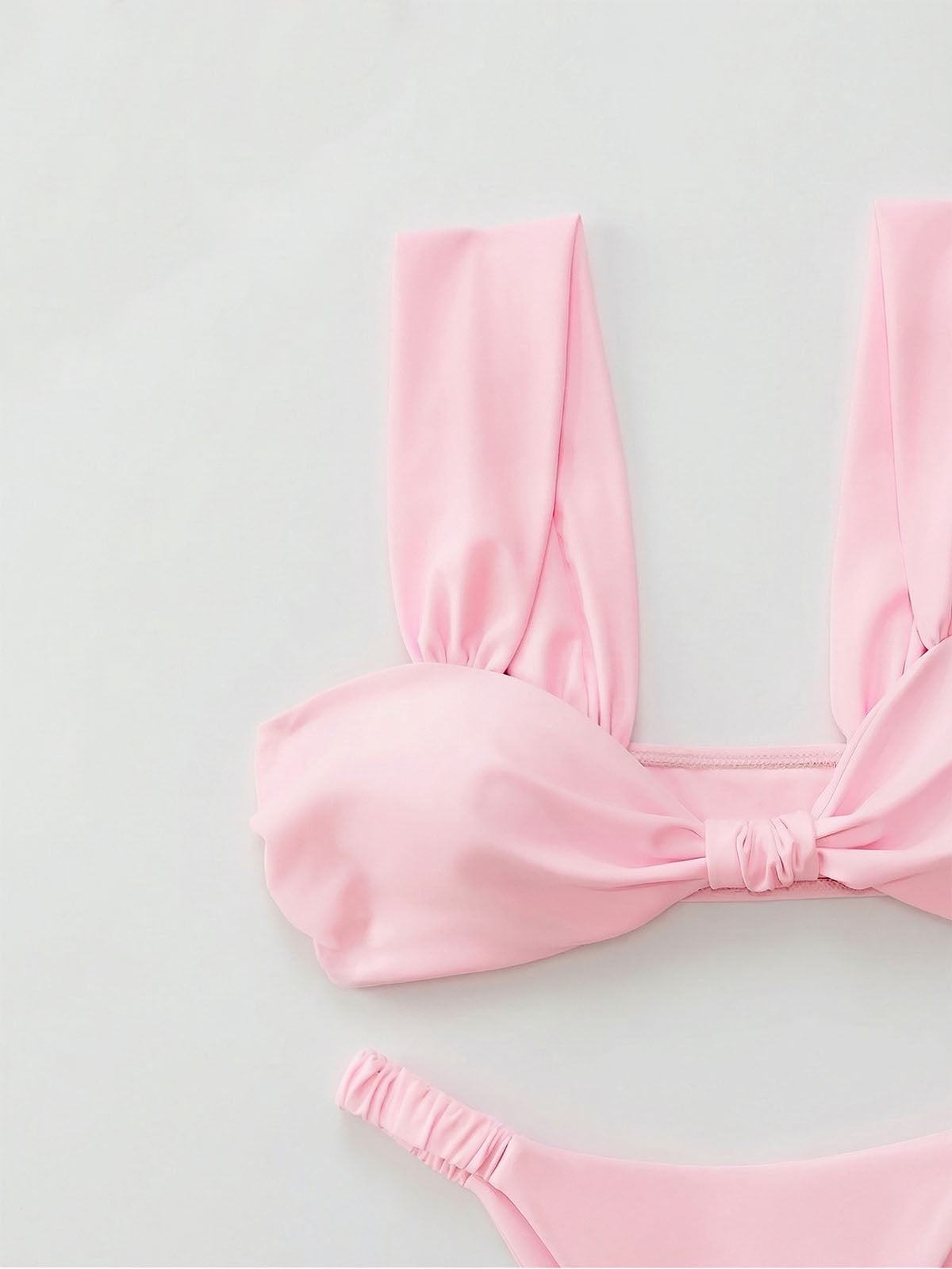 Close-up of a pink bikini top with a twisted knot detail and wide shoulder straps.