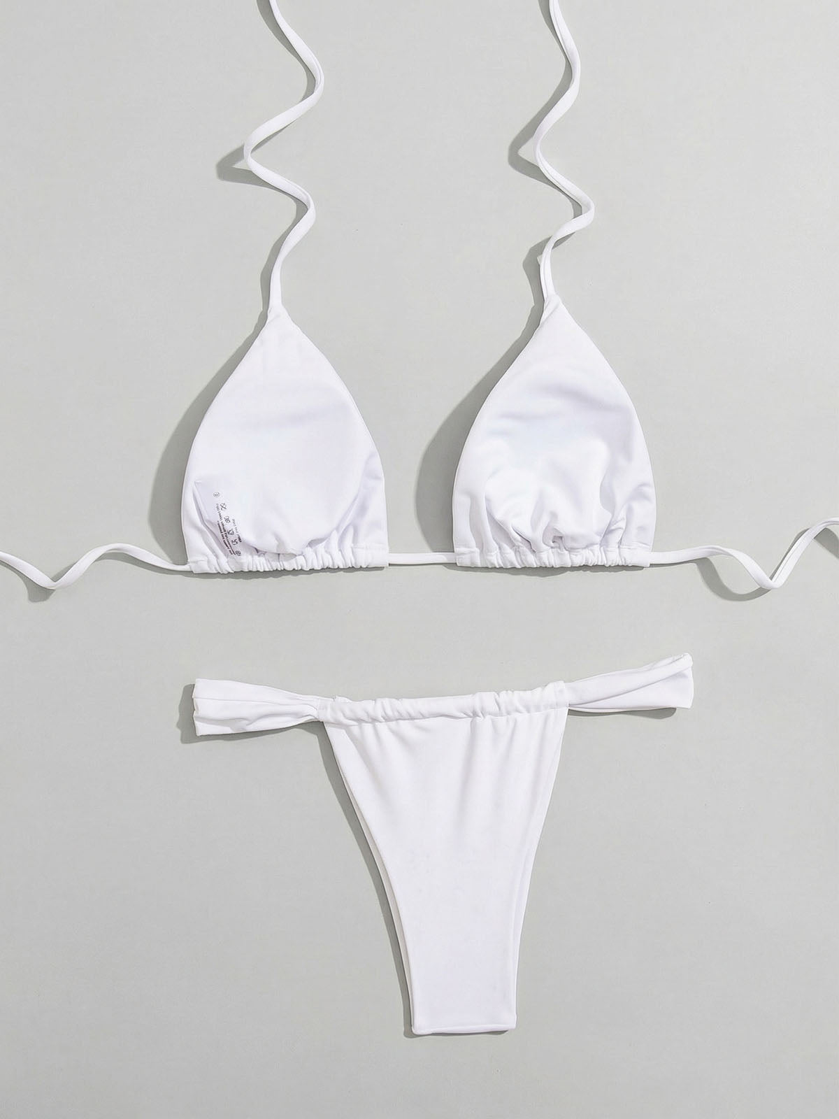 Back view of a white triangle bikini top and ruched thong bottoms laid flat