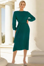 Woman wearing a long-sleeved green knit dress with a belted waist and pleated skirt
