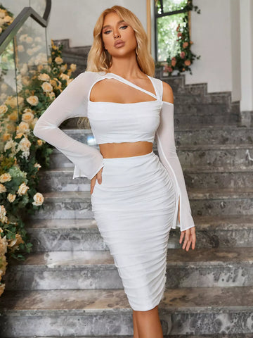 Woman in a white two-piece set with an asymmetrical crop top and ruched midi skirt, standing on a marble staircase.