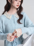 Close-up of a woman's chest wearing a light blue knit cardigan with a lace collar and lace cuffs.