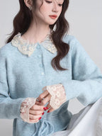 Close-up of a woman's chest wearing a light blue knit cardigan with a lace collar and lace cuffs.
