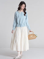 Full body shot of a woman wearing a light blue knit cardigan with a white tiered skirt and holding a woven basket.