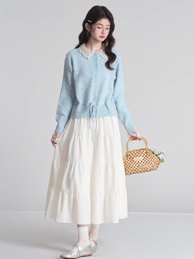 Full body shot of a woman wearing a light blue knit cardigan with a white tiered skirt and holding a woven basket.