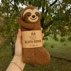 Hand holding a brown knit sock with a sloth design and 'Sloth Socks' label