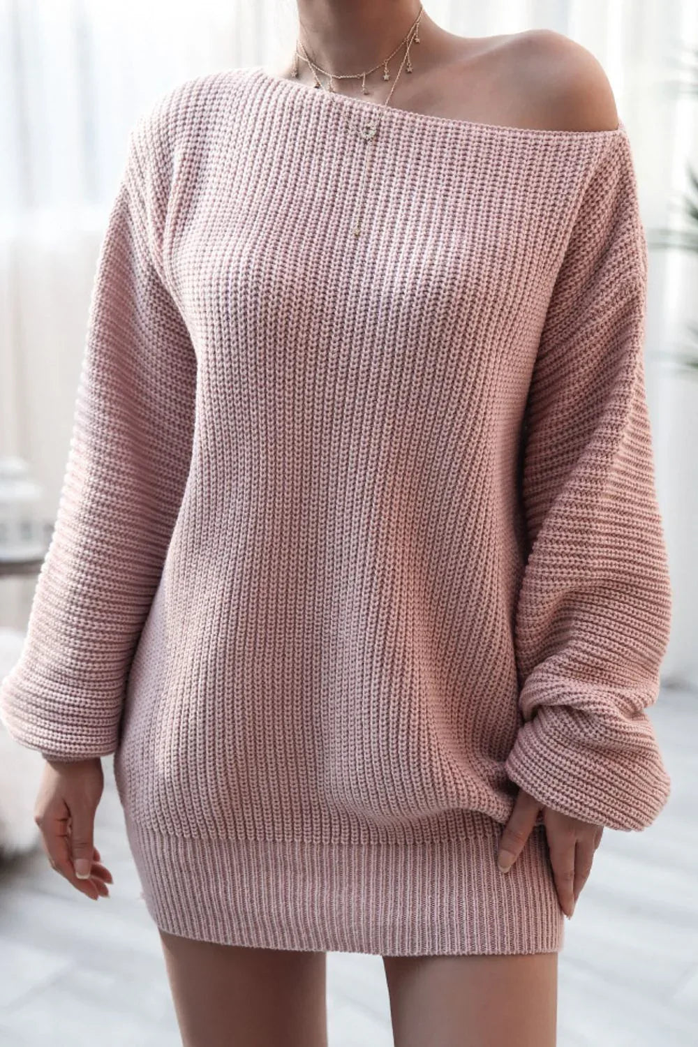 Woman wearing a pink off-the-shoulder knit tunic sweater
