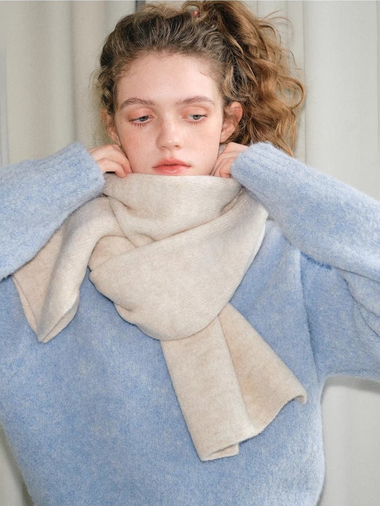 Woman wearing a light blue fuzzy sweater and a cream and beige two-tone knit scarf wrapped around her neck.