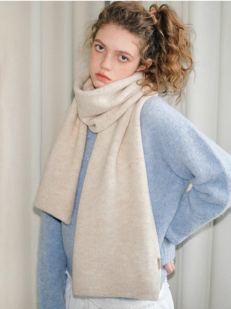 Woman posing with a cream and beige two-tone knit scarf over a light blue sweater.