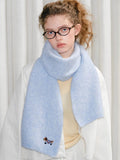 Woman wearing a light blue knit scarf with an embroidered dachshund graphic on one end.